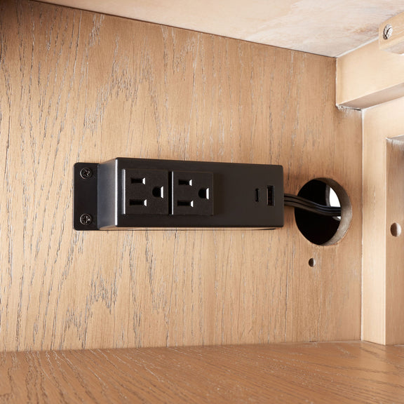 Black power strip with outlets mounted on beige wood panel