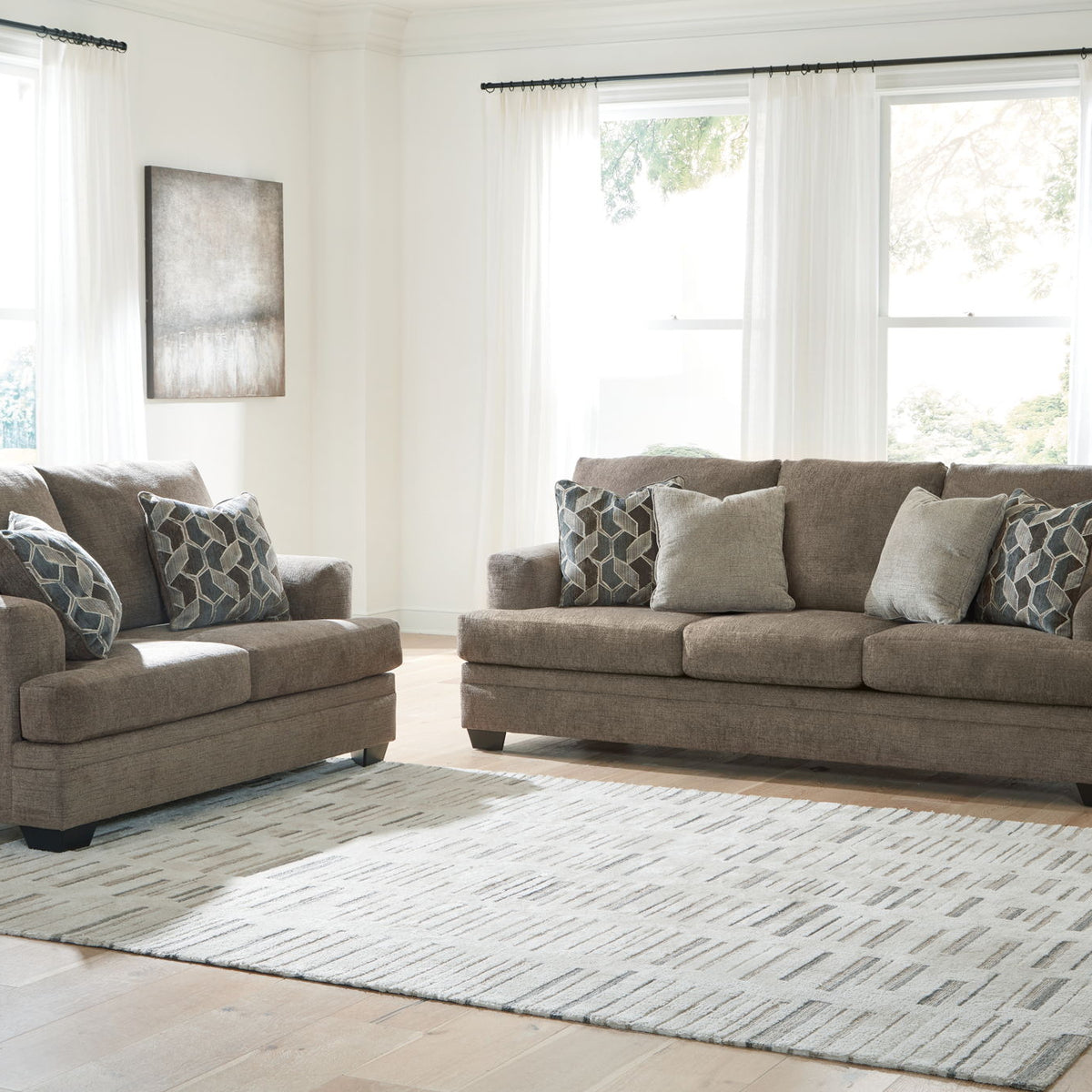Taupe fabric sofa set with matching chair and seat ottoman, staged on a patterned rug.