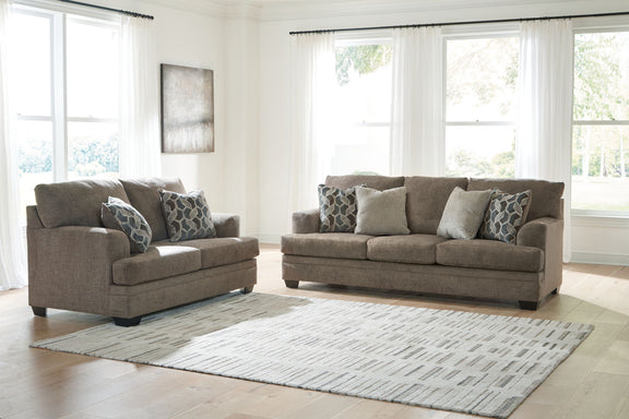 Taupe fabric sofa set with matching chair and seat ottoman, staged on a patterned rug.