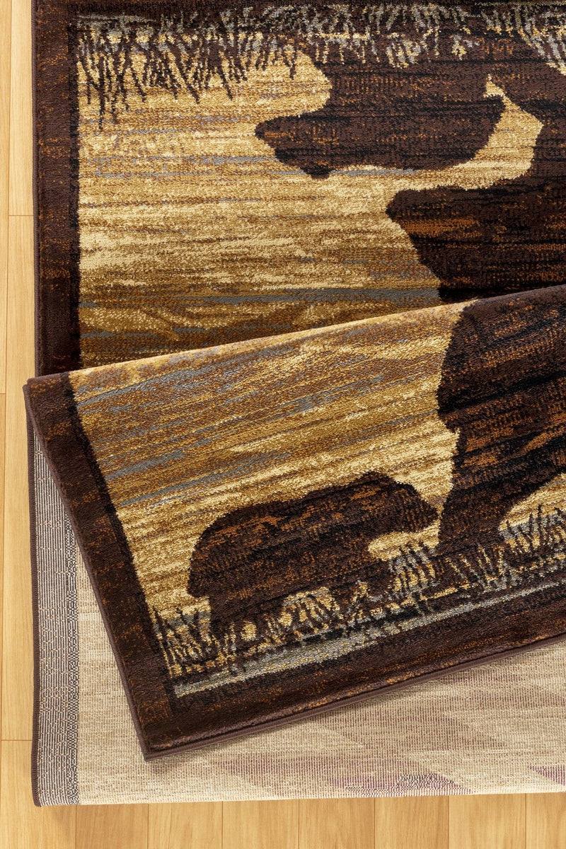 Beige lodge area rug angled view with dark brown motifs, border, and scattered shapes