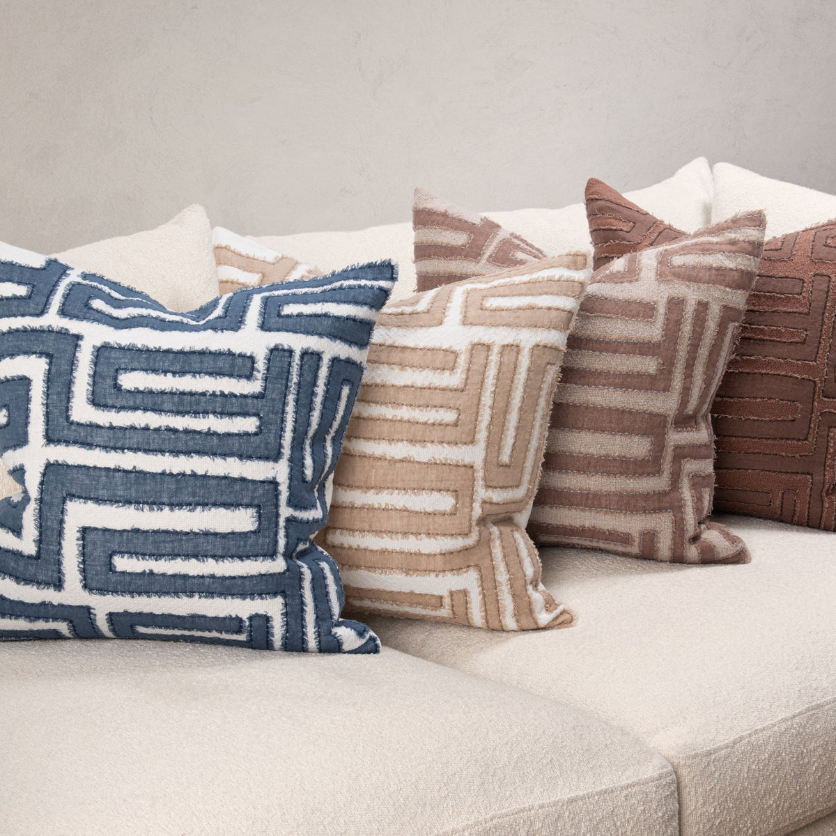 Decorative pillows with geometric maze patterns in navy, tan, and brown on a sofa