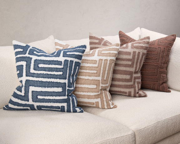 Decorative pillows with geometric maze patterns in navy, tan, and brown on a sofa