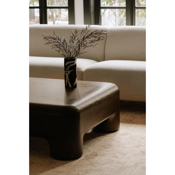 Dark brown coffee table corner with smooth rounded edges and thick pedestal legs.