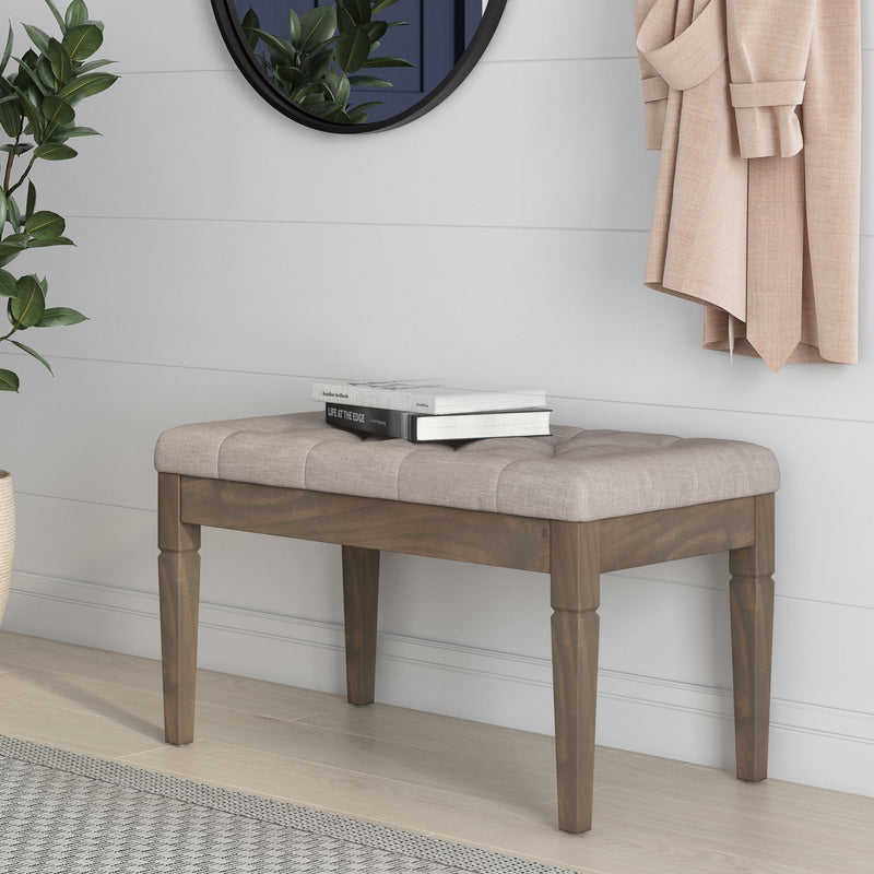Gray upholstered ottoman bench with dark wooden legs and tufted seat top