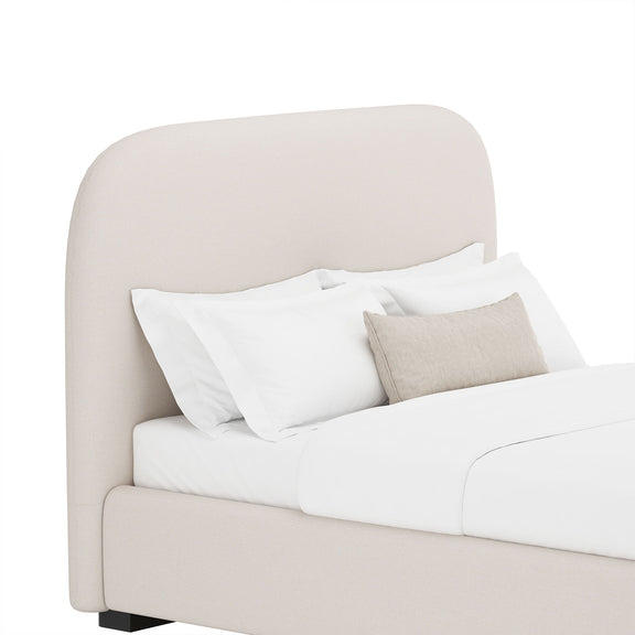 Beige upholstered bed with rounded headboard and side panels, styled with pillows