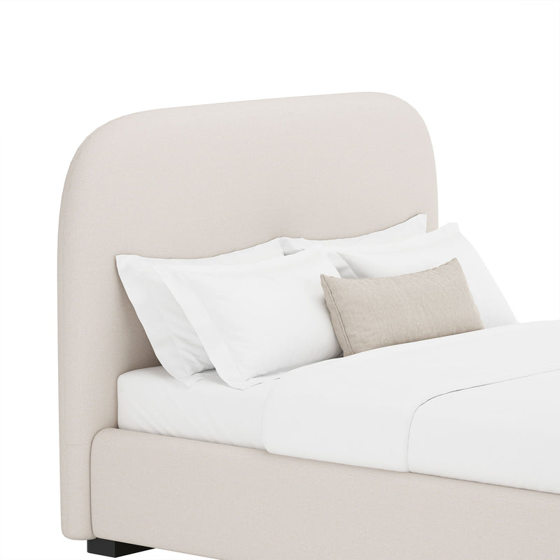 Beige upholstered bed with rounded headboard and side panels, styled with pillows