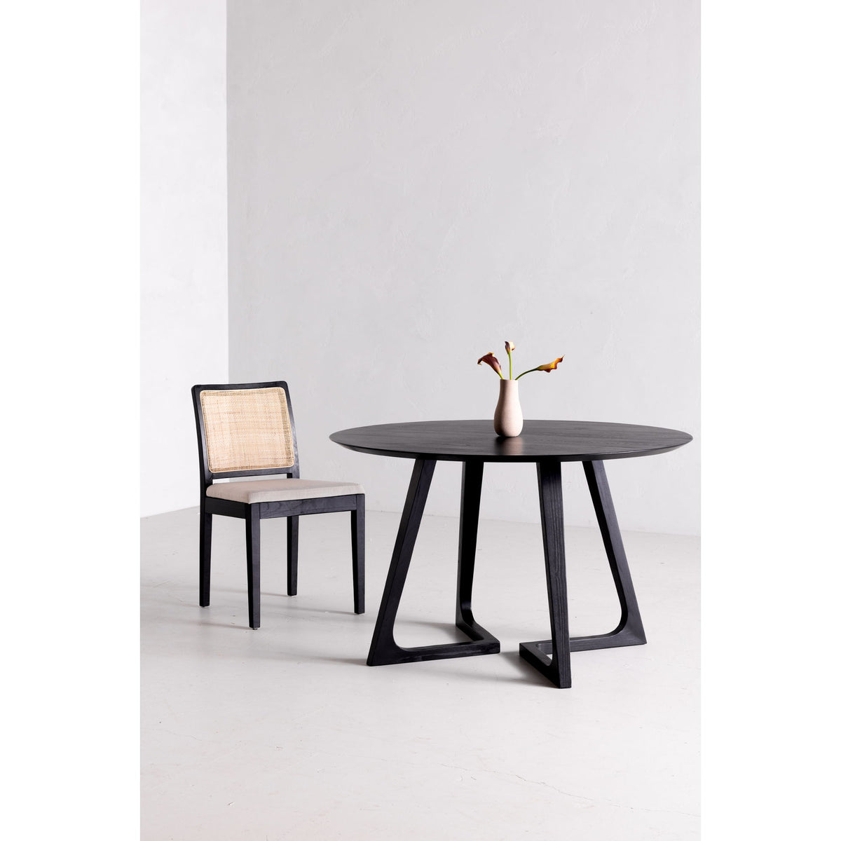 Round dining table with dark tabletop and four-sided pedestal base with X cutouts