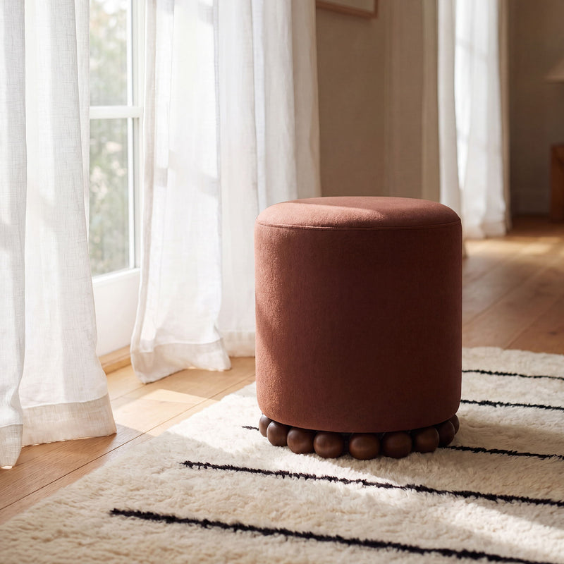 Rust-brown round ottoman with beaded wooden base in a living room setting