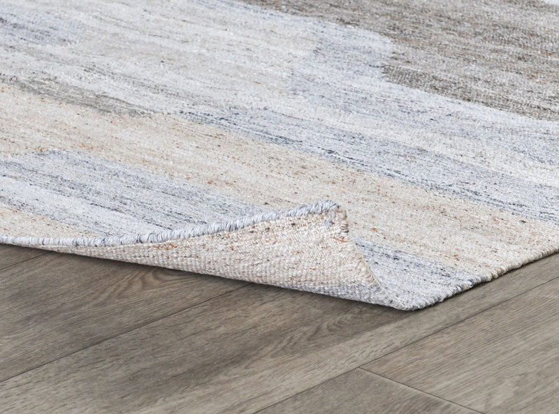 Corner detail of sand-and-gray indoor/outdoor rug with textured weave and stitched edge