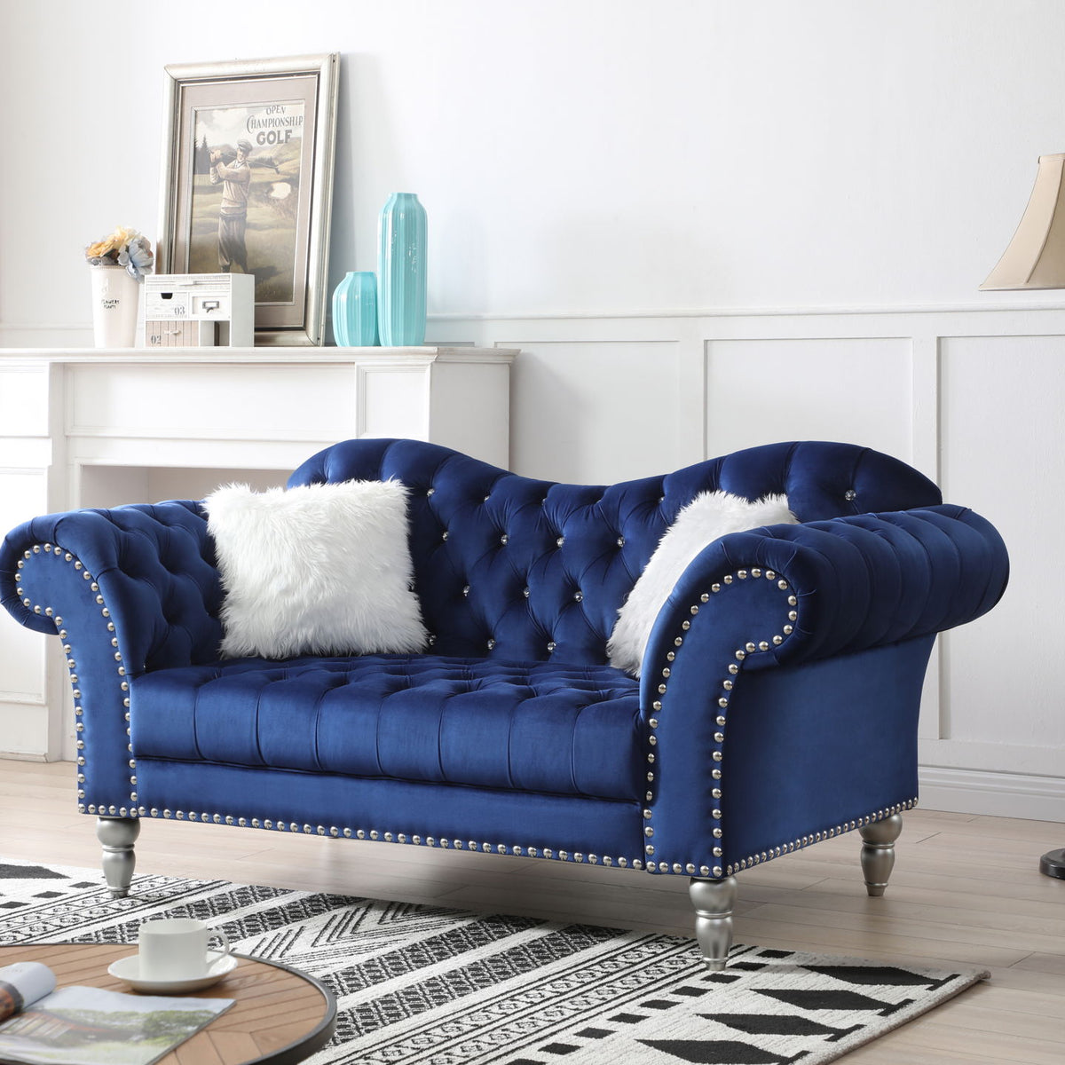 Blue velvet round arm loveseat with tufted back, nailhead trim, and two white faux fur pillows.