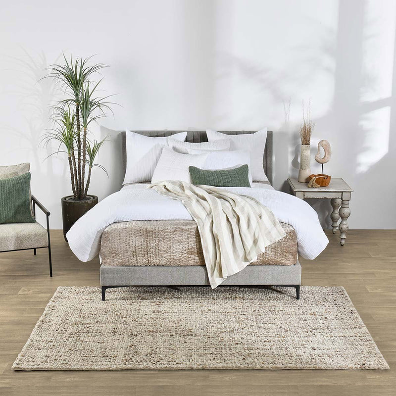 Natural wool area rug in a bedroom setting, textured weave with fringe border