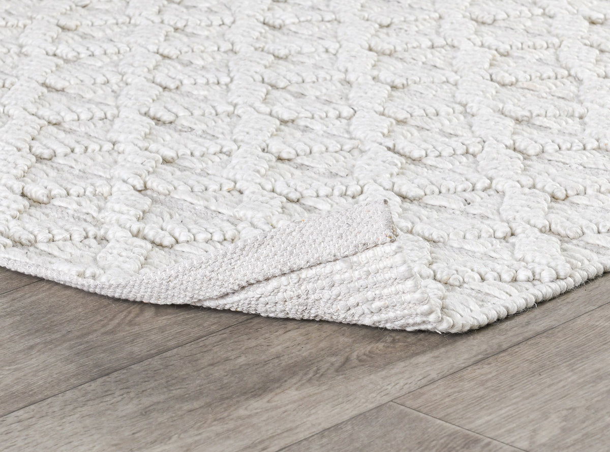 Ivory textured area rug corner with raised loop pattern and stitched border.