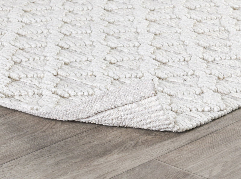 Ivory textured area rug corner with raised loop pattern and stitched border.