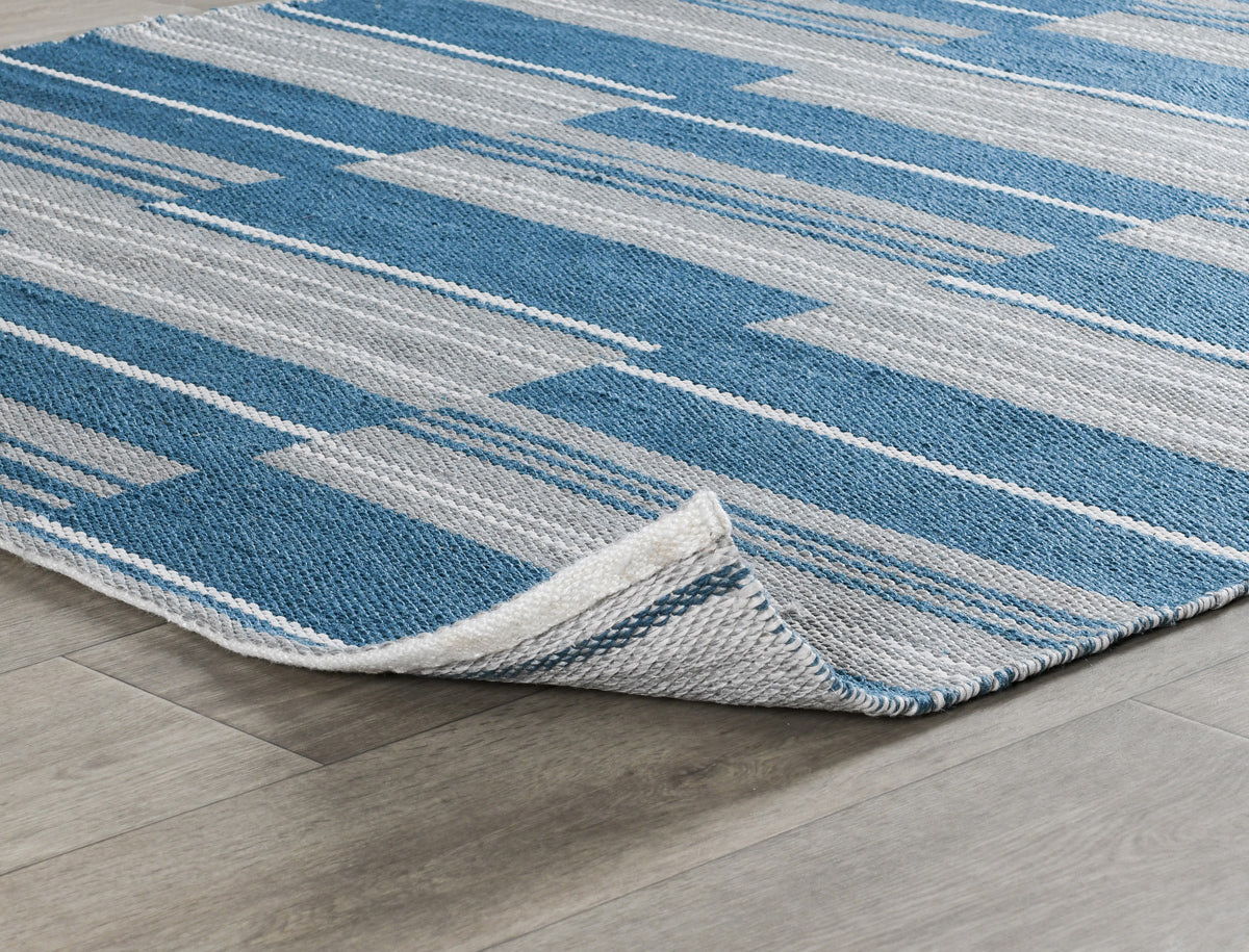 Indoor/outdoor striped rug corner with blue and ivory horizontal lines and bound edge