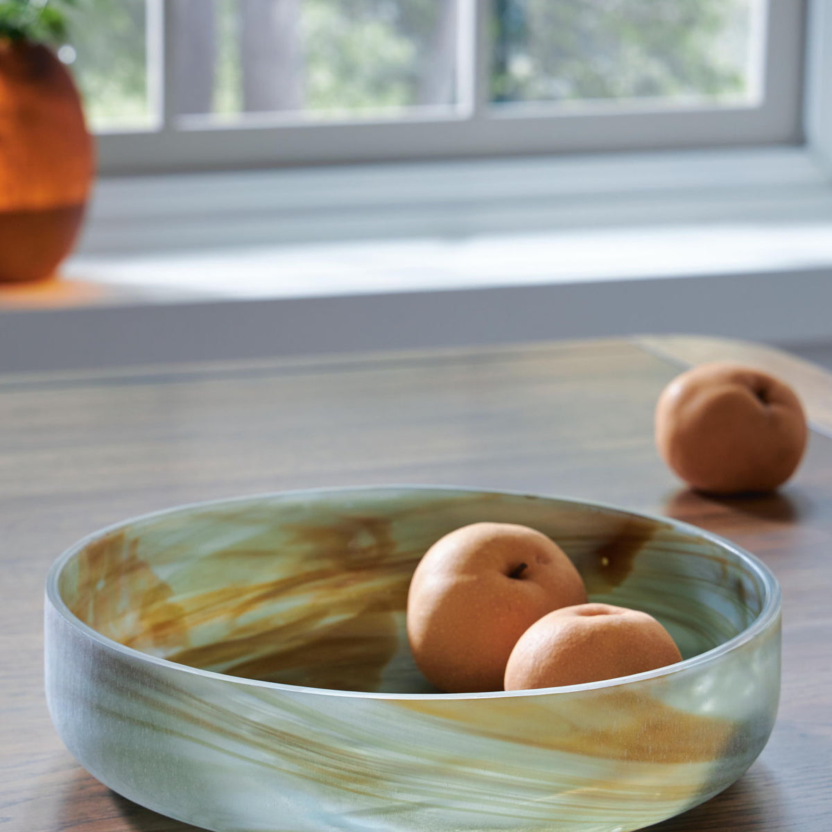 Sage green glass bowl with three orange decorative balls on a tabletop