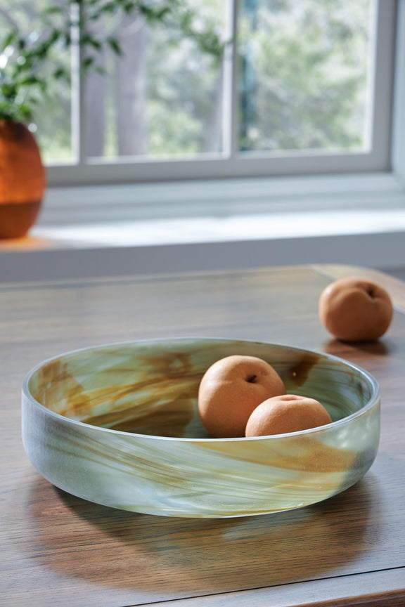 Sage green glass bowl with three orange decorative balls on a tabletop
