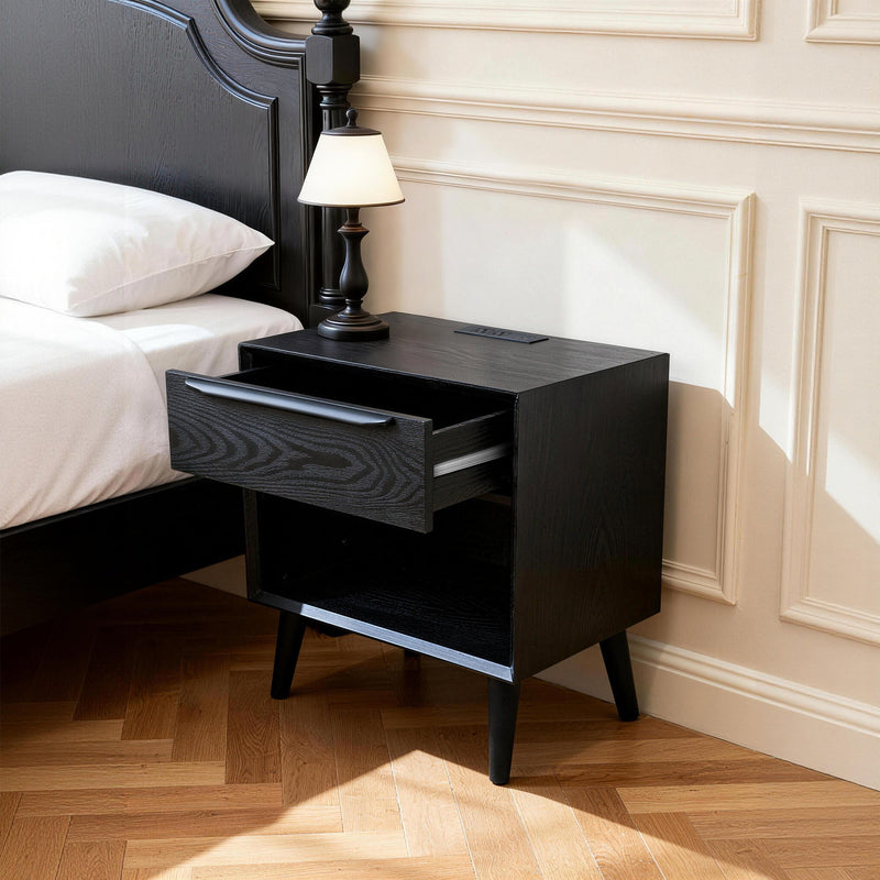 Black bedside table with 1 drawer pulled open, open shelf, tapered legs