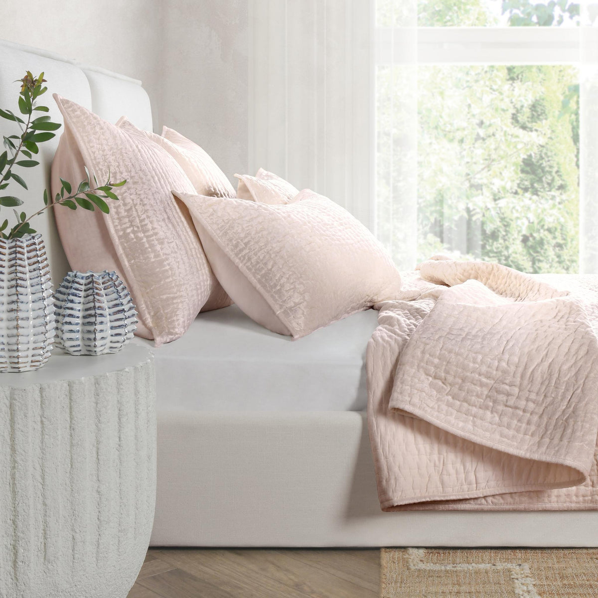 Blush pink velvet quilt set with textured quilt and pillow shams on sofa.