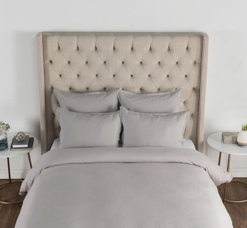 Pair of light gray solid sham pillows against a tufted headboard