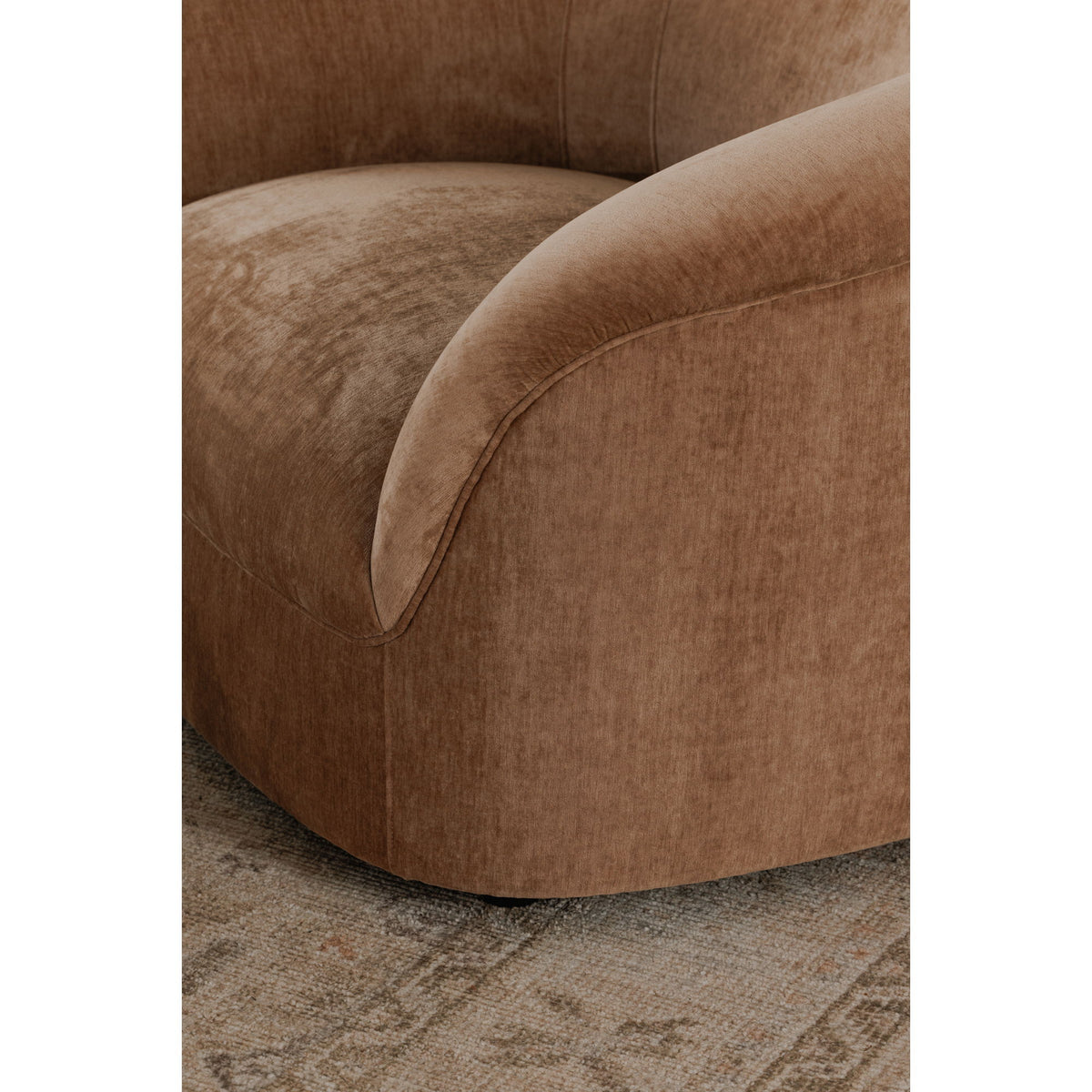 Blush upholstered lounge chair arm and seat with curved trim and plush cushion.