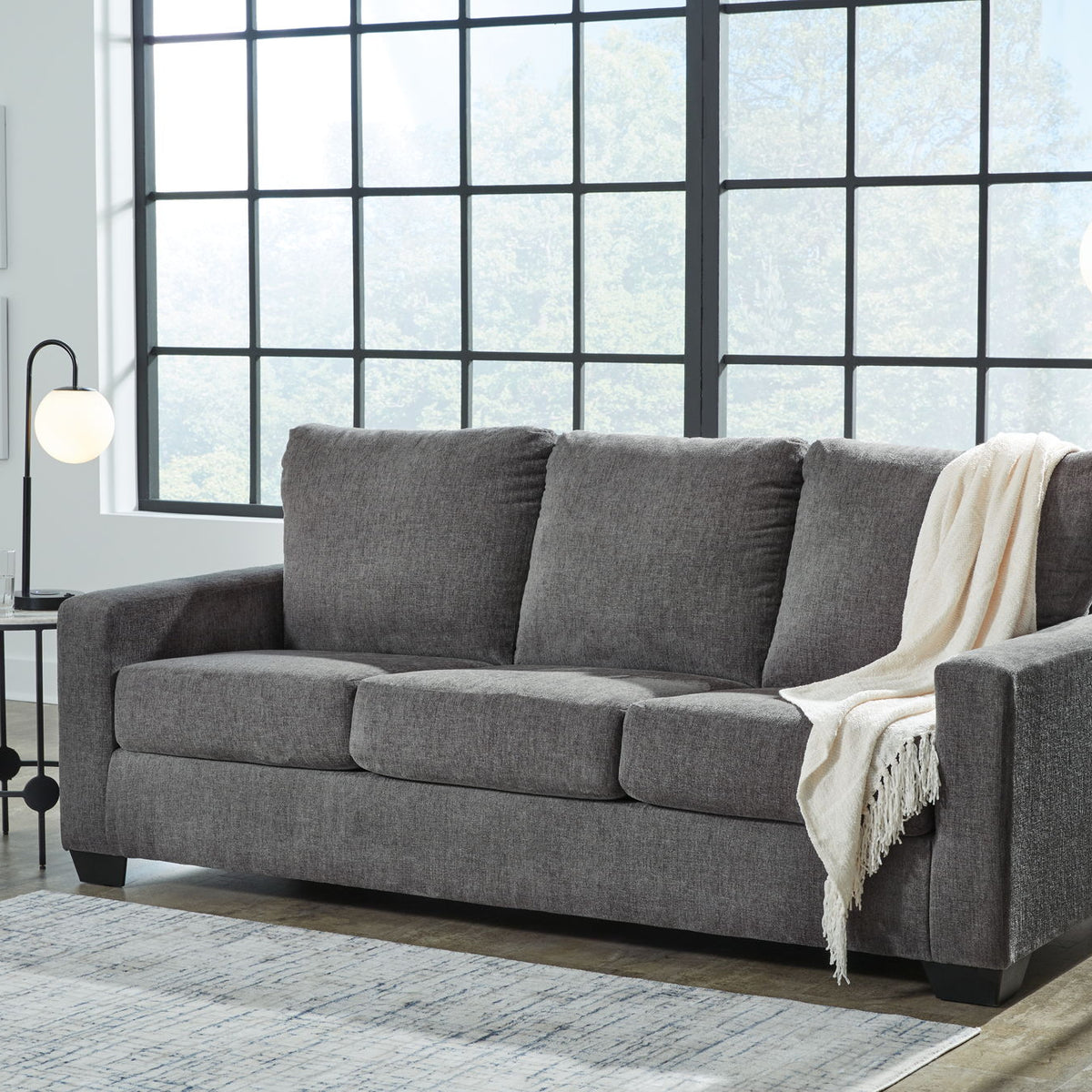 Gray fabric sofa with three seat cushions and white blanket draped over arm