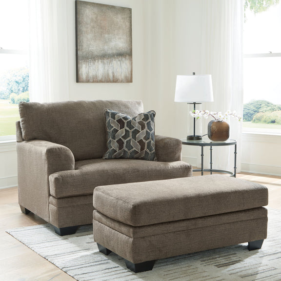 Taupe fabric loveseat-style chair with matching ottoman, styled with decorative pillows.