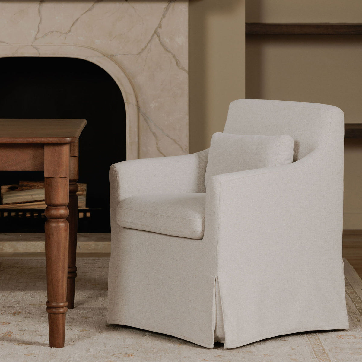 Beige slipcovered dining chair with curved arms and backrest, side angle