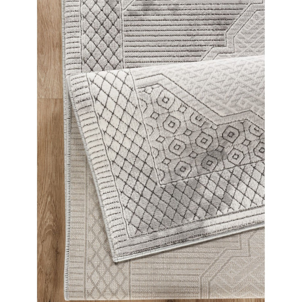 Gray geometric rug corner with stitched border and raised diamond texture