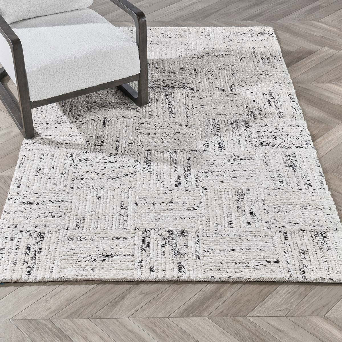Ivory distressed area rug shown in room with textured blocks and dark gray accents