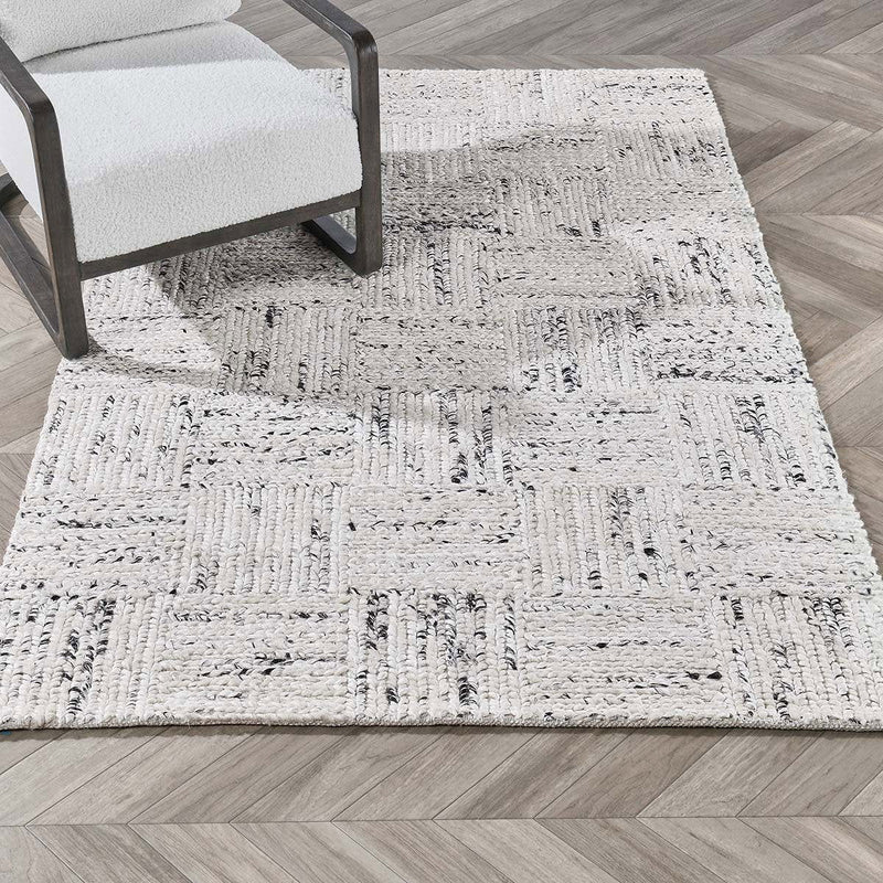 Ivory distressed area rug shown in room with textured blocks and dark gray accents