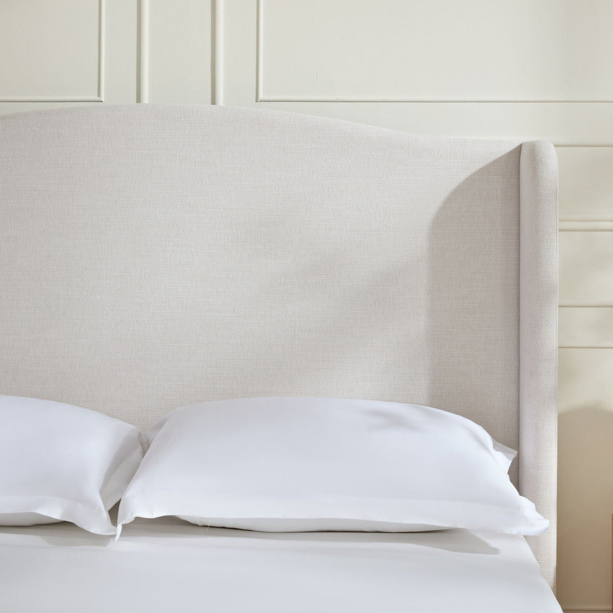 Beige tall upholstered wingback headboard with smooth fabric and curved sides