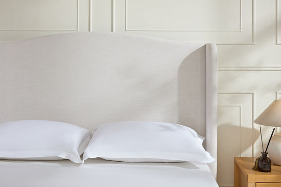 Beige tall upholstered wingback headboard with smooth fabric and curved sides