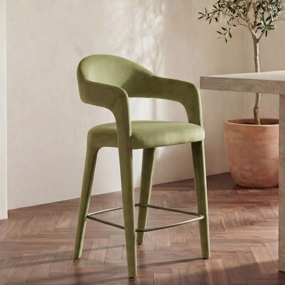 Green velvet counter stool with curved back and arms, metal base with ring footrest.