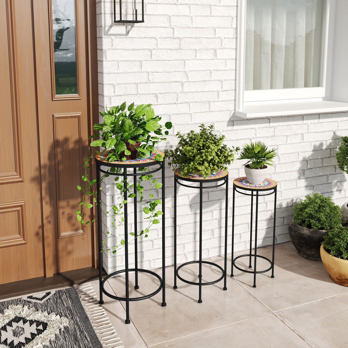 Three black metal plant stands with round patterned tops holding potted plants