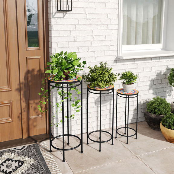 Three black metal plant stands with round patterned tops holding potted plants