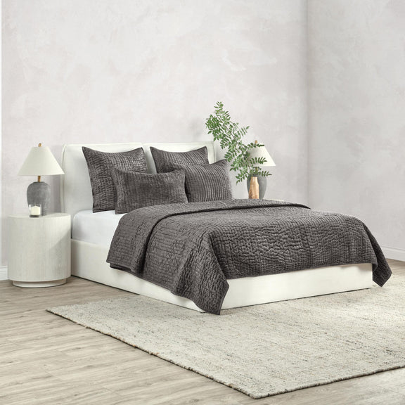 Dark gray velvet quilt set with textured quilt and matching shams on a bed