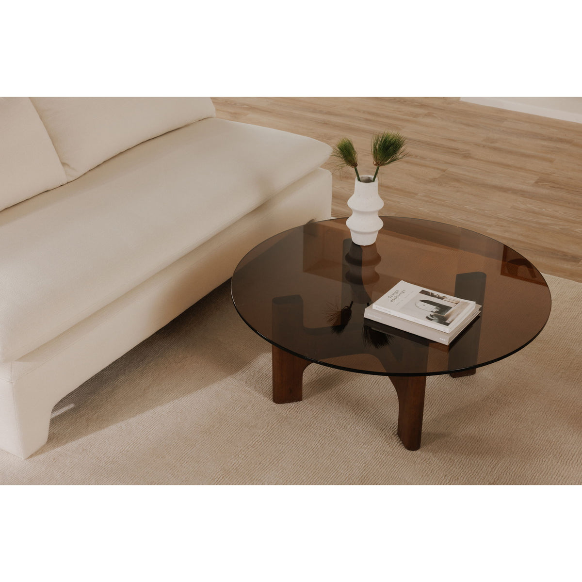 Round glass coffee table with dark brown wooden legs holding a vase