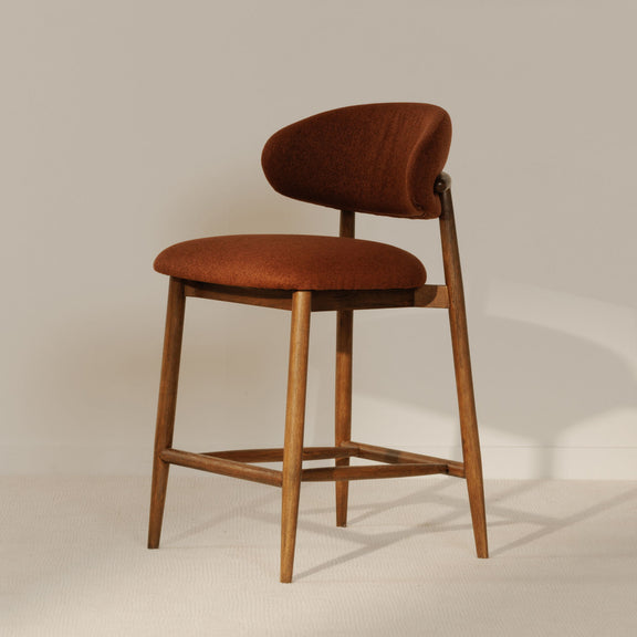 Rust upholstered counter stool with curved backrest, padded seat, light wood legs and bar