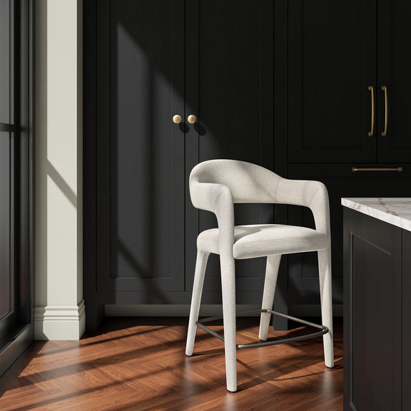 Beige upholstered counter stool with curved arms and a metal footrest, shown at an angle