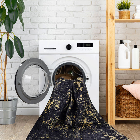 Washable dark navy area rug with gold speckles draped on open washer door