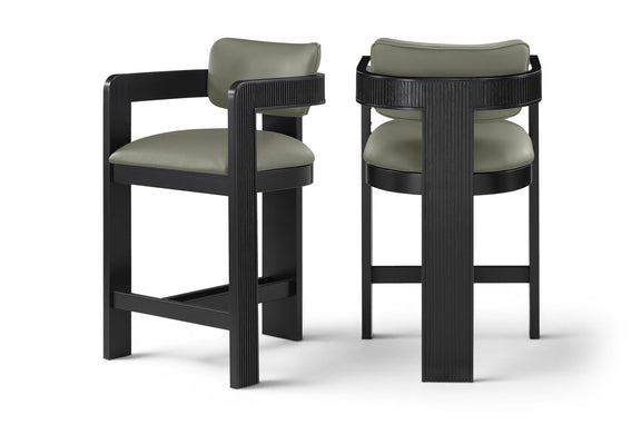 Two vegan leather counter stools with light green upholstered seats and black ribbed frames