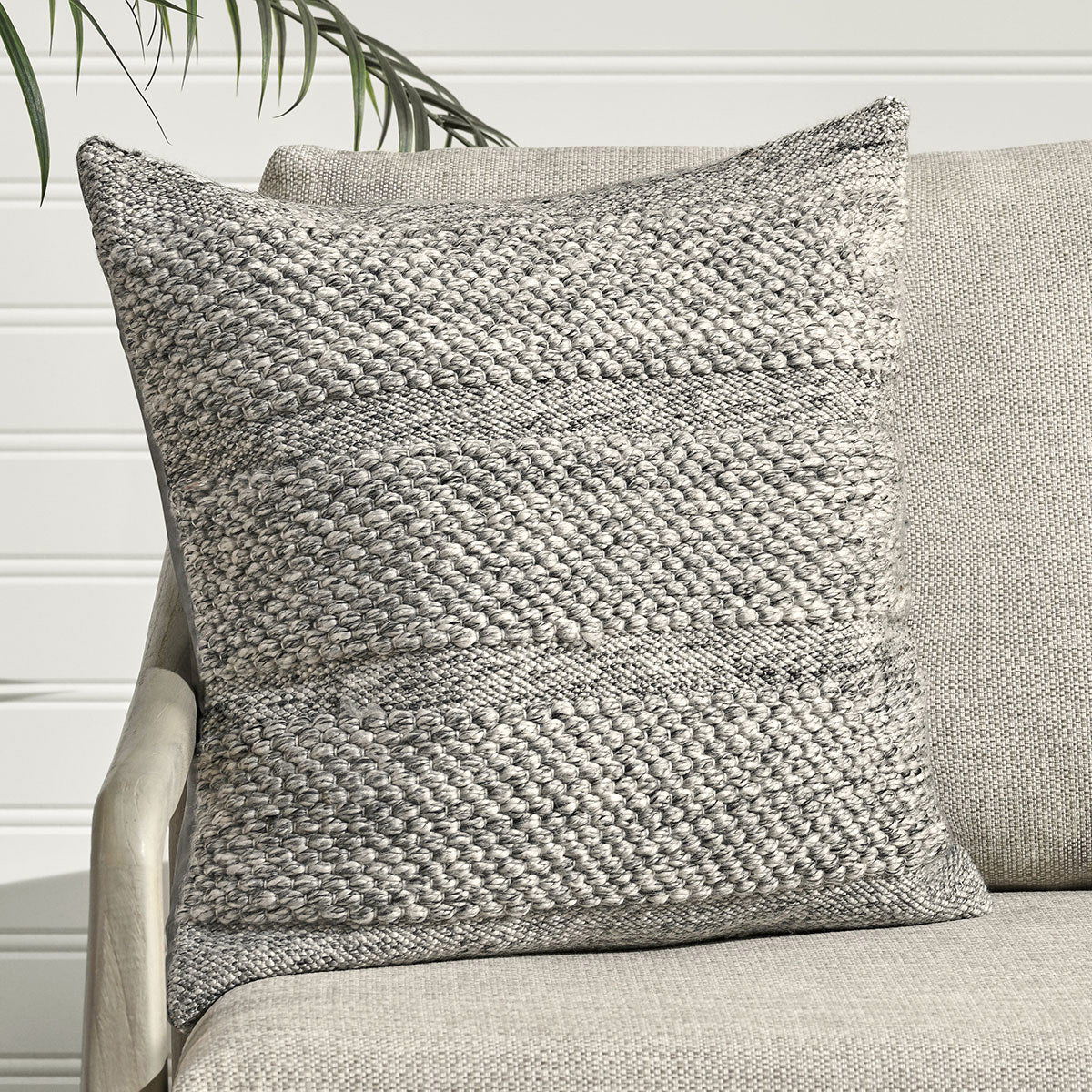 Gray woven throw pillow on a sofa, square shape with loop texture and seam details.