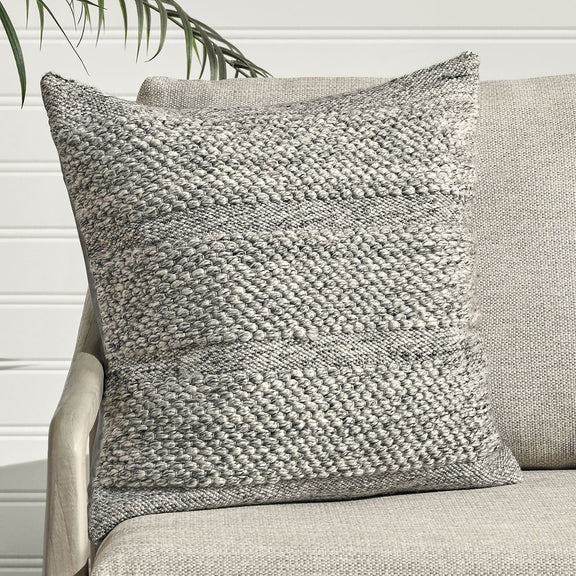 Gray woven throw pillow on a sofa, square shape with loop texture and seam details.