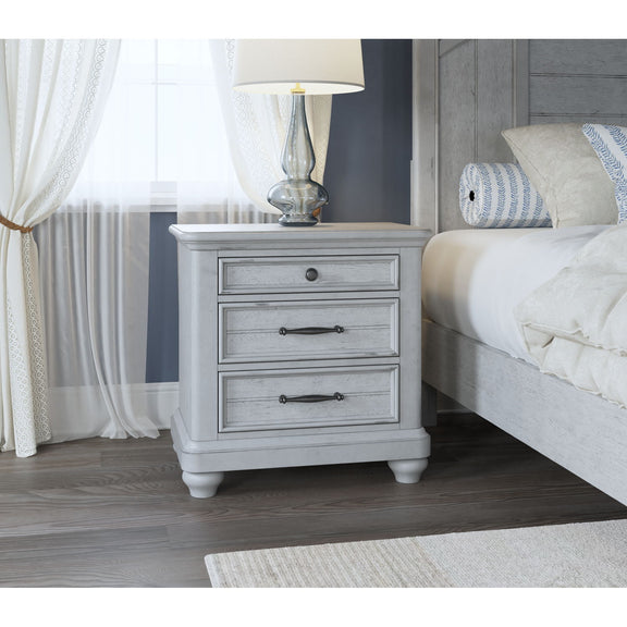 Gray wood 3-drawer nightstand with metal pulls and turned legs beside bed.