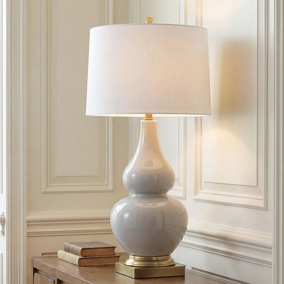 Cream fabric table lamp shade over glossy gray ceramic body with gold base