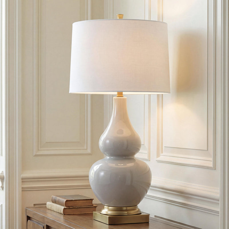 Cream fabric table lamp shade over glossy gray ceramic body with gold base