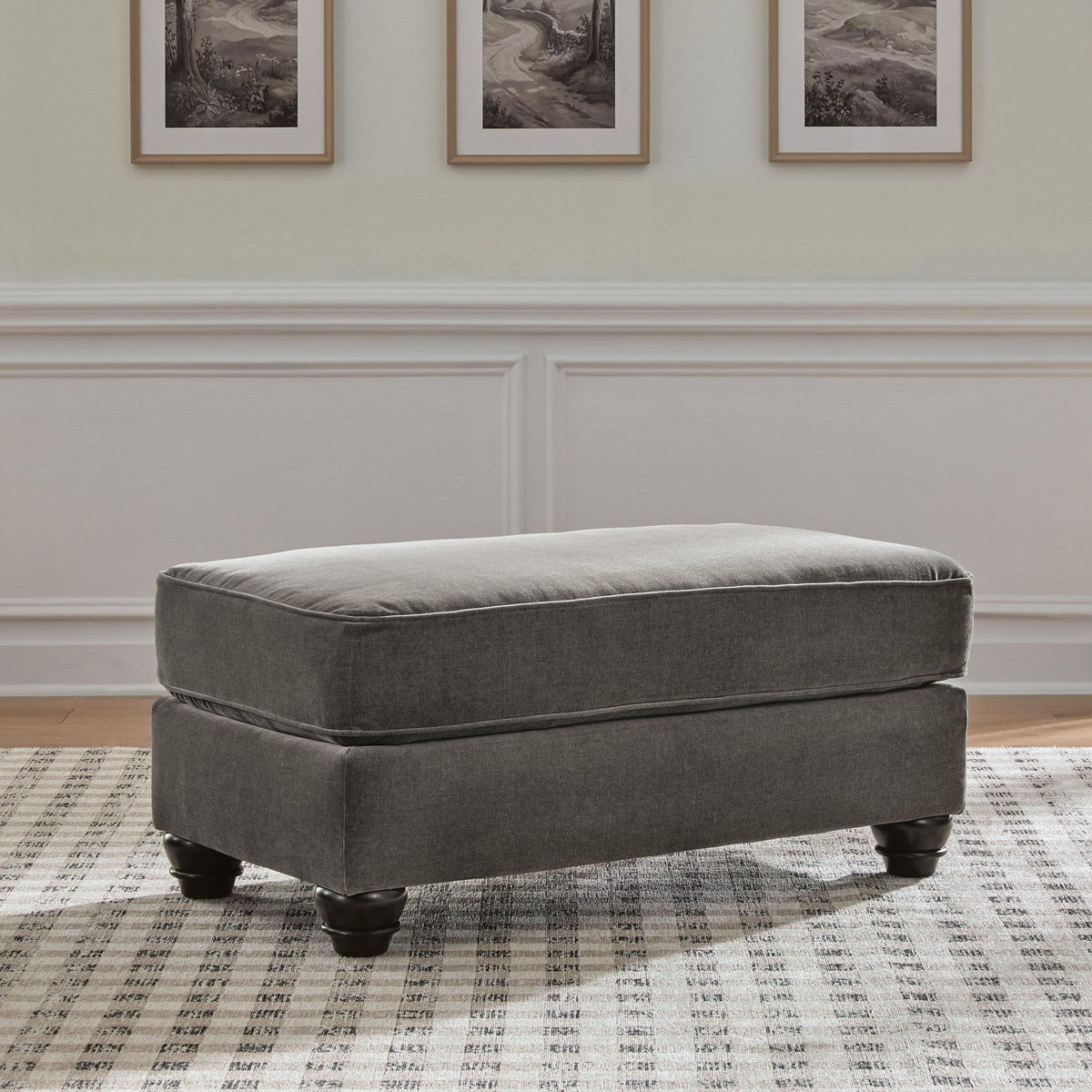 Dark gray upholstered ottoman with padded seat and turned wooden legs