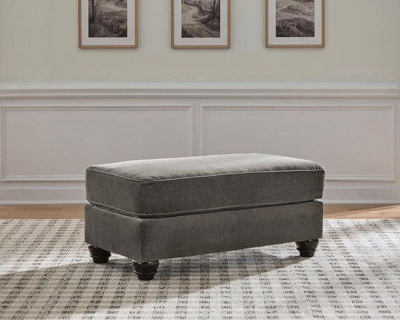 Dark gray upholstered ottoman with padded seat and turned wooden legs