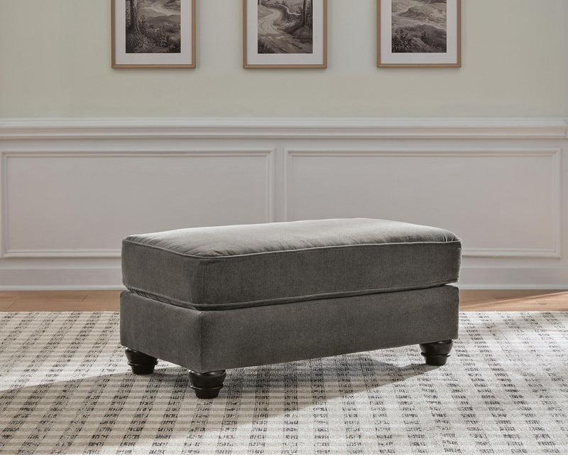 Dark gray upholstered ottoman with padded seat and turned wooden legs