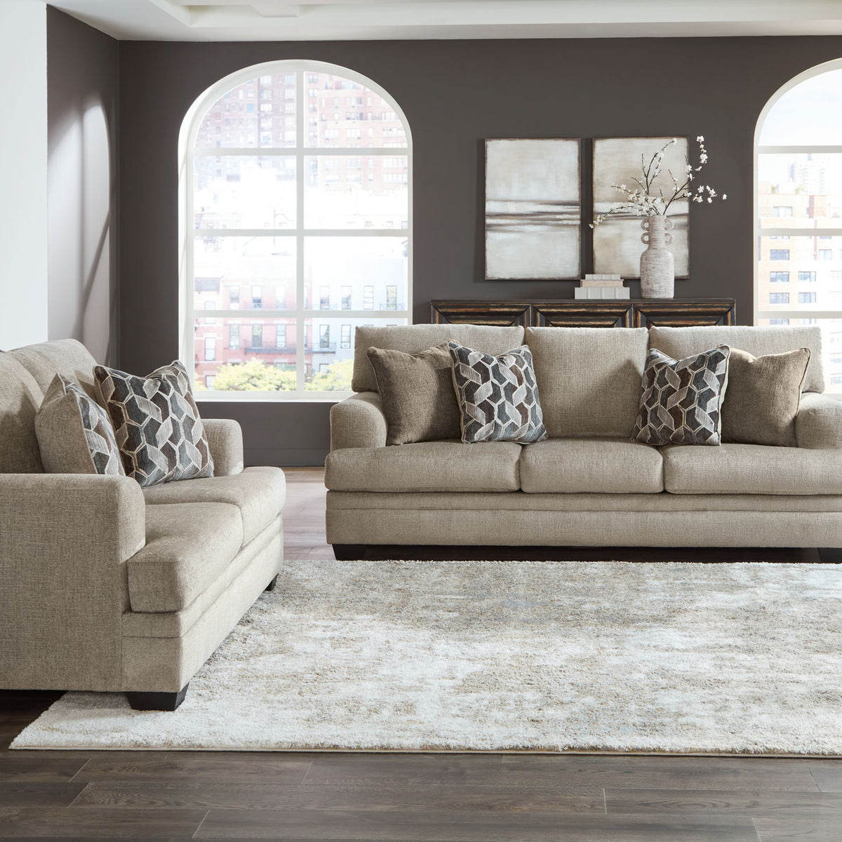 Taupe fabric sofa set with chaise chair and ottoman, arranged around a large area rug.